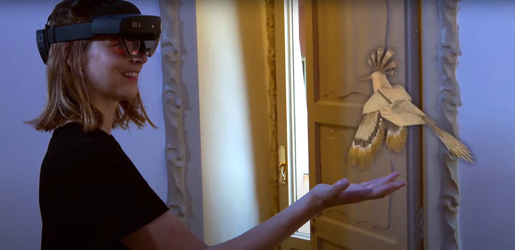 Visitor wearing HoloLens 2 holding out her hand to a paper bird hologram
